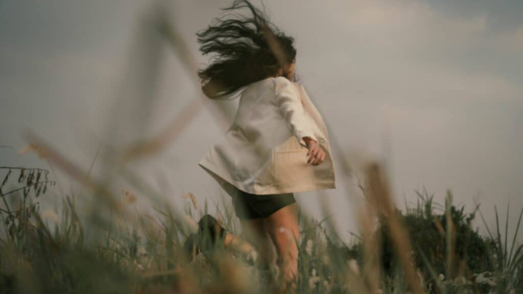 Uma mulher correndo num gramado denso.