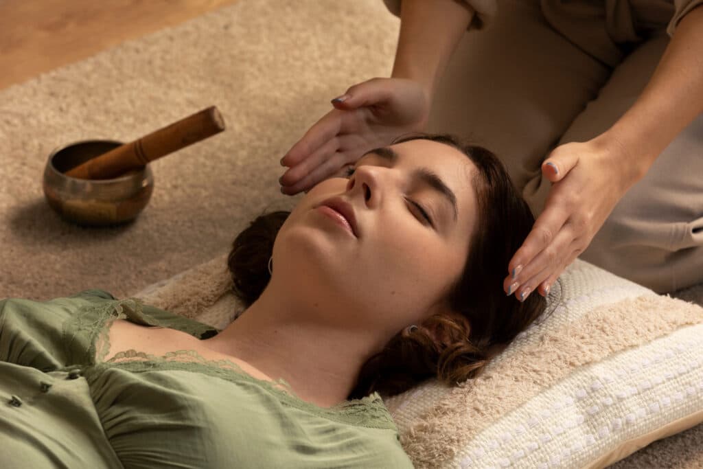 Mulher branca de cabelos escuros deitada sob o chão, recebendo a terapia de reiki.