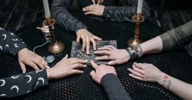 Várias mãos tocando um tabuleiro místico na mesa redonda
