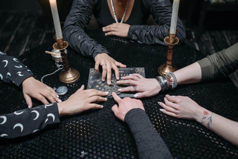 Várias mãos tocando um tabuleiro místico na mesa redonda