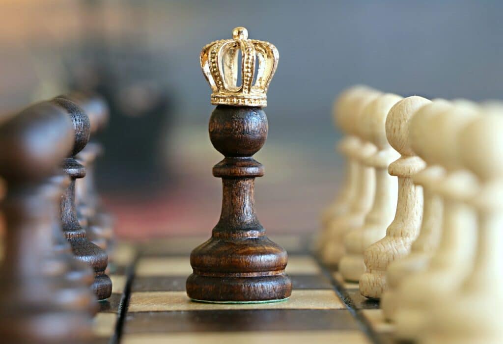Peão com coroa de rei no meio do tabuleiro de xadrez e em meio a outros peões pequenos 