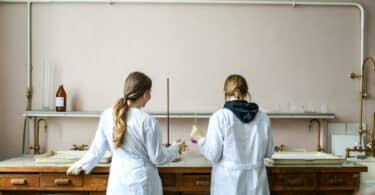 Duas mulheres de jaleco fazendo experimentos numa bancada