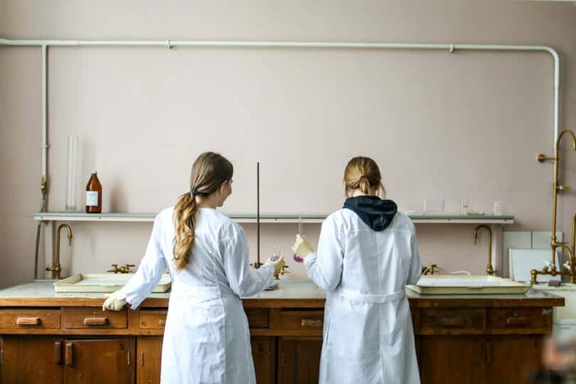 Duas mulheres de jaleco fazendo experimentos numa bancada