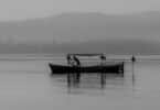 Imagem preto e branco de um barco isolado no meio da água com um pescador