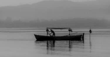 Imagem preto e branco de um barco isolado no meio da água com um pescador