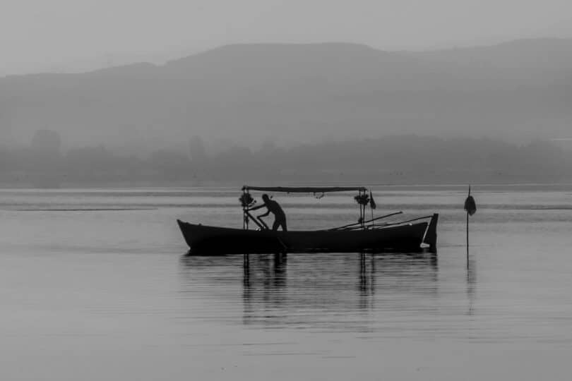 Imagem preto e branco de um barco isolado no meio da água com um pescador