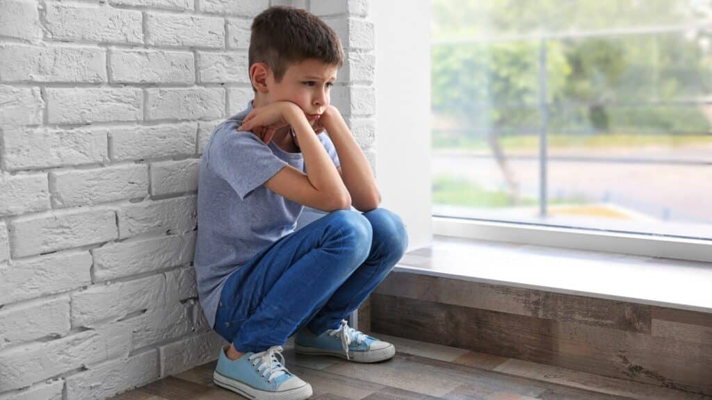 Um garoto triste de joelhos à beira de uma janela.