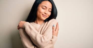 Jovem mulher bonita vestindo suéter casual sobre fundo branco isolado Abraçando-se feliz e positivo, sorrindo confiante. Amor próprio e autocuidado