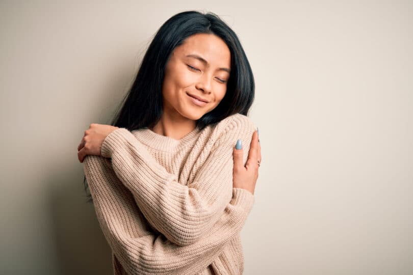 Jovem mulher bonita vestindo suéter casual sobre fundo branco isolado Abraçando-se feliz e positivo, sorrindo confiante. Amor próprio e autocuidado