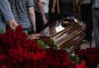 Imagem de caixão rodeado de flores e pessoas se despedindo