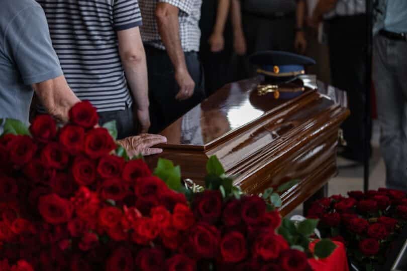 Imagem de caixão rodeado de flores e pessoas se despedindo