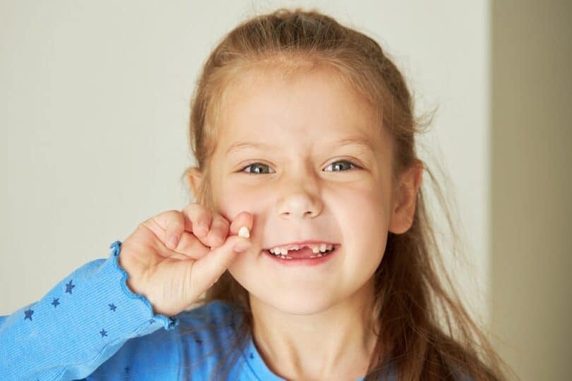 Garotinha segurando um dente caído. Ela está sorridente.