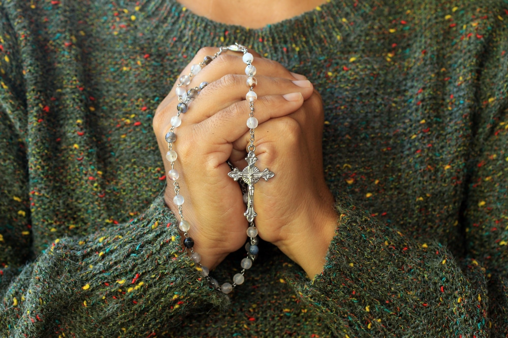Mãos femininas unidas em oração e segurando um terço.