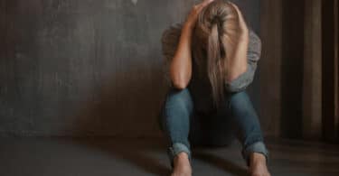 Mulher sentada no chão, com a cabeça abaixada e segurando-a com as mãos em sinal de desespero.