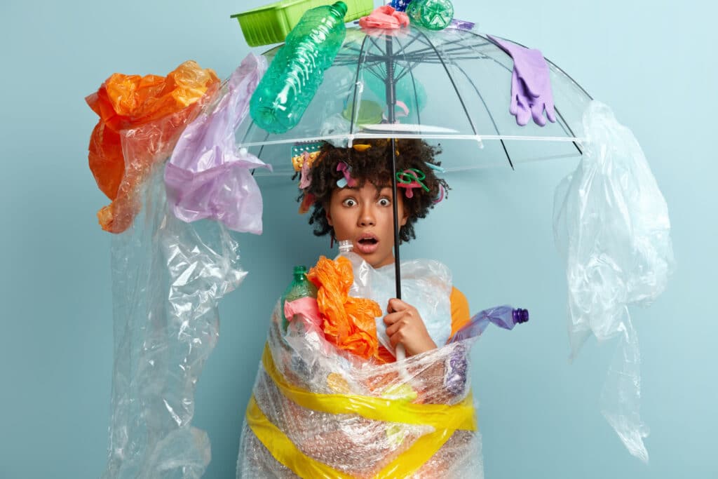 Mulher negra segurando um guarda-chuva enrolada por sacolas plásticas e lixo.