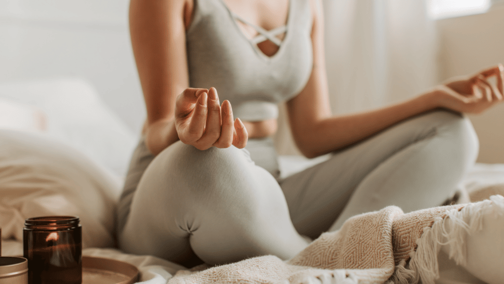 Mulher meditando em cima da cama, com vela aromática acesa. 