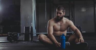 Imagem de um homem musculoso na academia sentado no chão e de cabeça baixa.