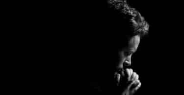 Imagem de um homem orando em um ambiente escuro