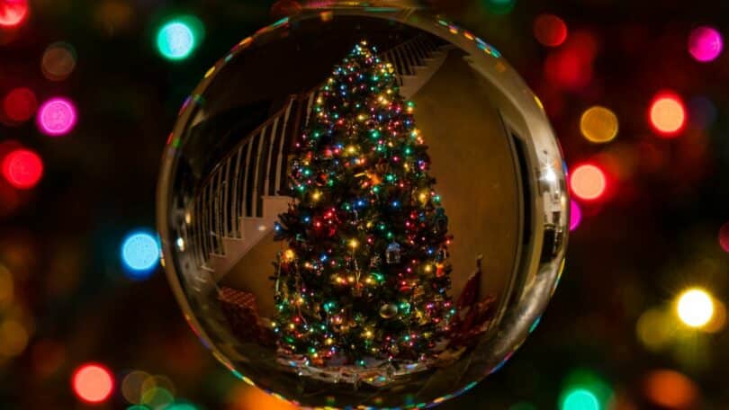 Imagem de uma árvore de natal refletida em um dos enfeites e luzes do pisca-pisca de fundo
