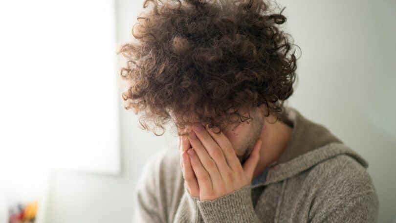 Imagem de um rapaz de cabelos cacheados com as mãos no rosto como se estivesse preocupado