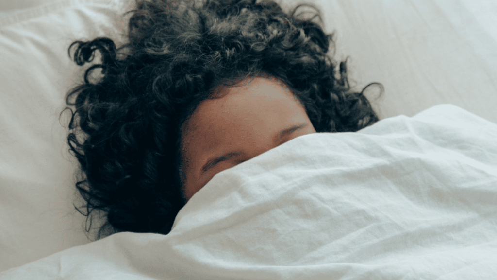 Imagem de uma moça com os olhos cobertos por um lençol na cama.