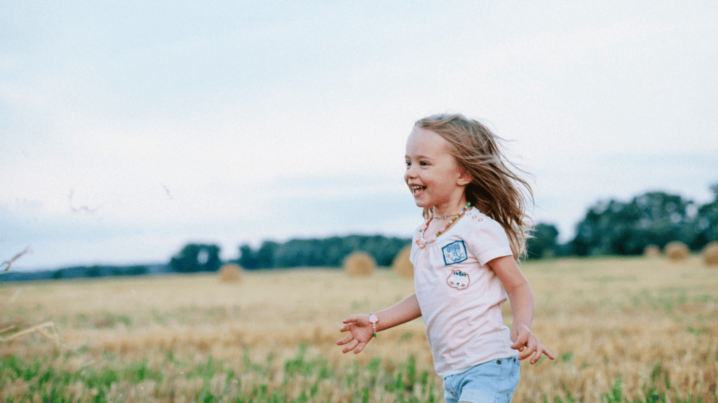 Criança sorrindo e correndo em um campo.