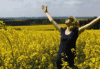 mulher com os braços erguidos e sorrindo em um campo cheio de flores amarelas.