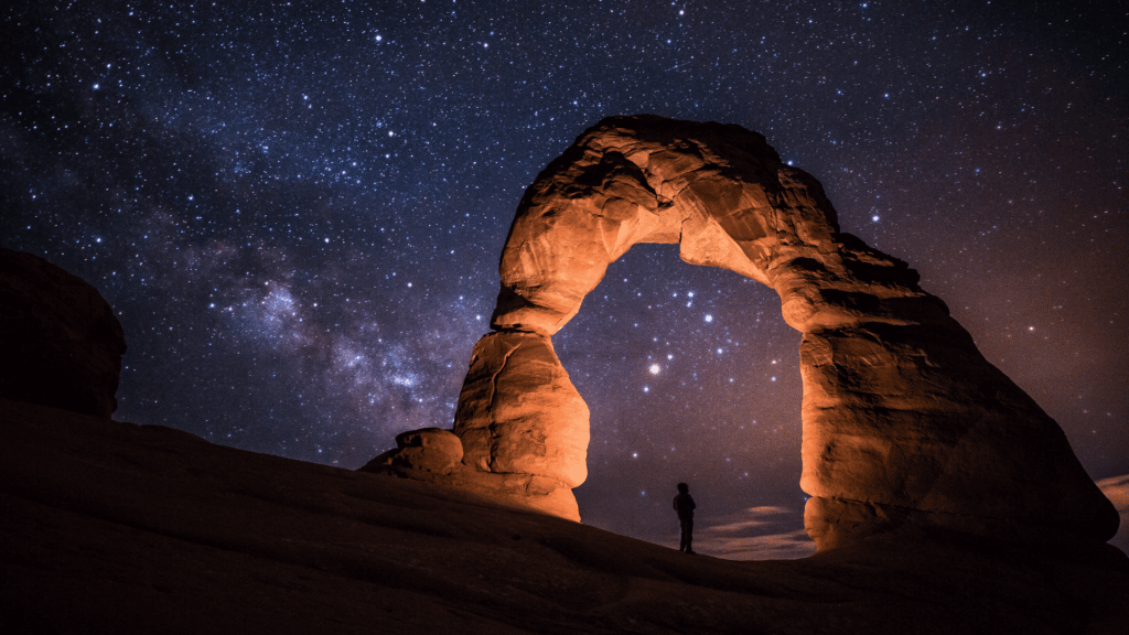 Pessoa em meio a arco de pedras e ao fundo, o céu estrelado. 