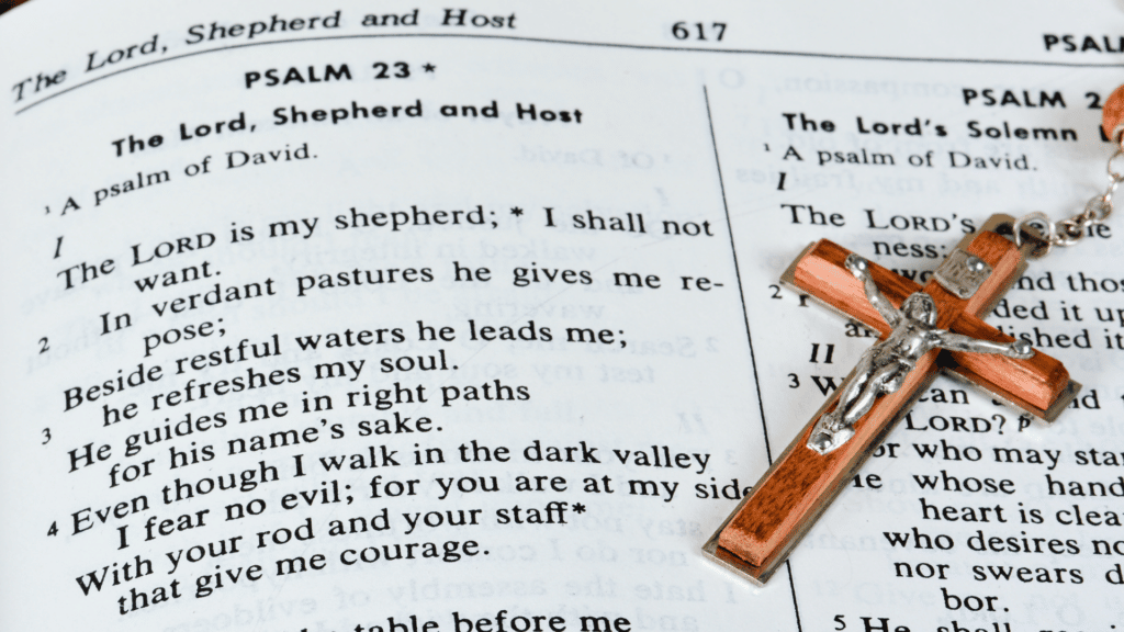 Foto de uma página da Bíblia, no Salmos ao lado de um crucifixo. 