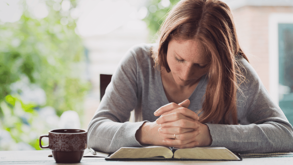 Mulher ruiva fazendo sua oração matinal apoiada na Bíblia.