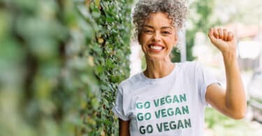 Uma mulher sorridente portando uma camiseta cuja inscrição é a frase "go vegan".