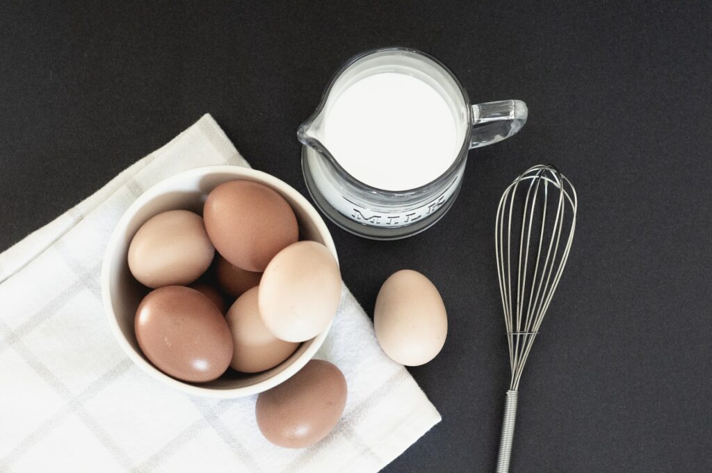 Pequeno recipiente sobre um pano, com ovos brancos e marrons dentro. Ao lado, uma jarra de leite e um fuê.