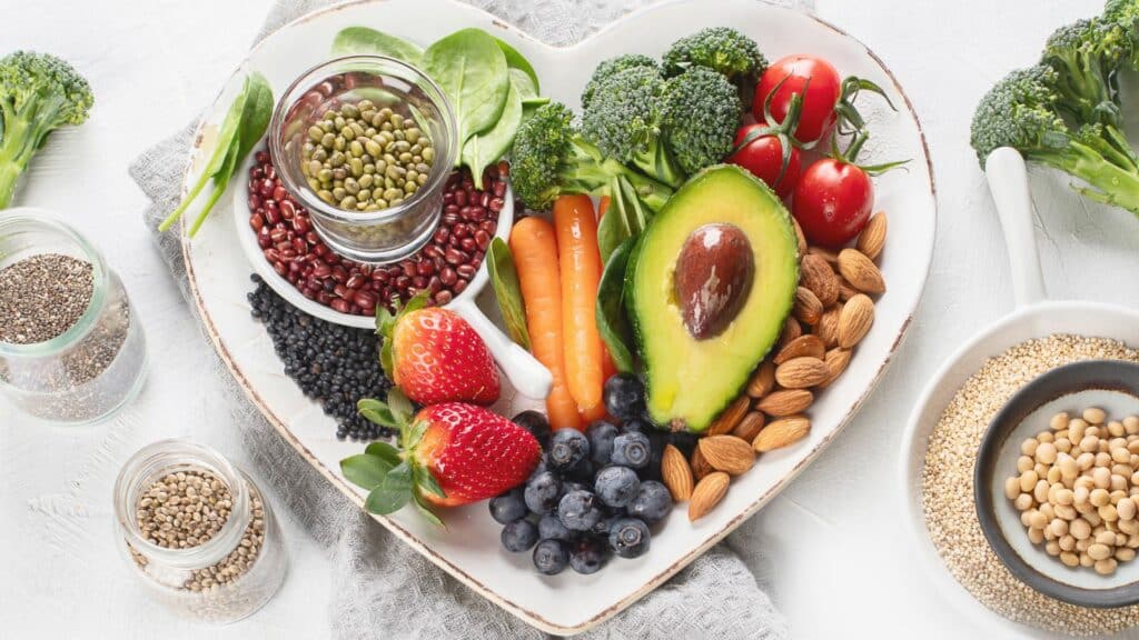 Grãos, frutas, vegetais, legumes e outros alimentos de origem vegetal dispostos numa mesa.