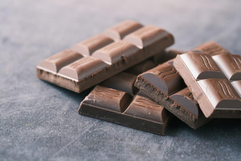 Quatro barras de chocolate ao leite sobrepostas uma à outra, sobre uma superfície plana.