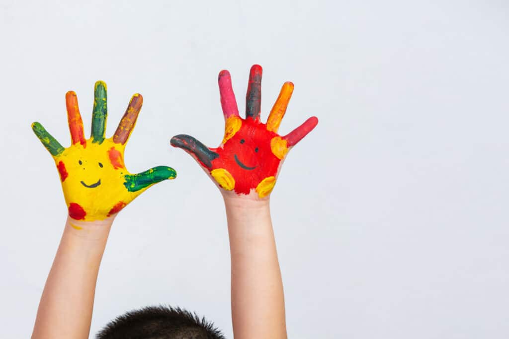 Mãos de criança pintadas com um rosto feliz.