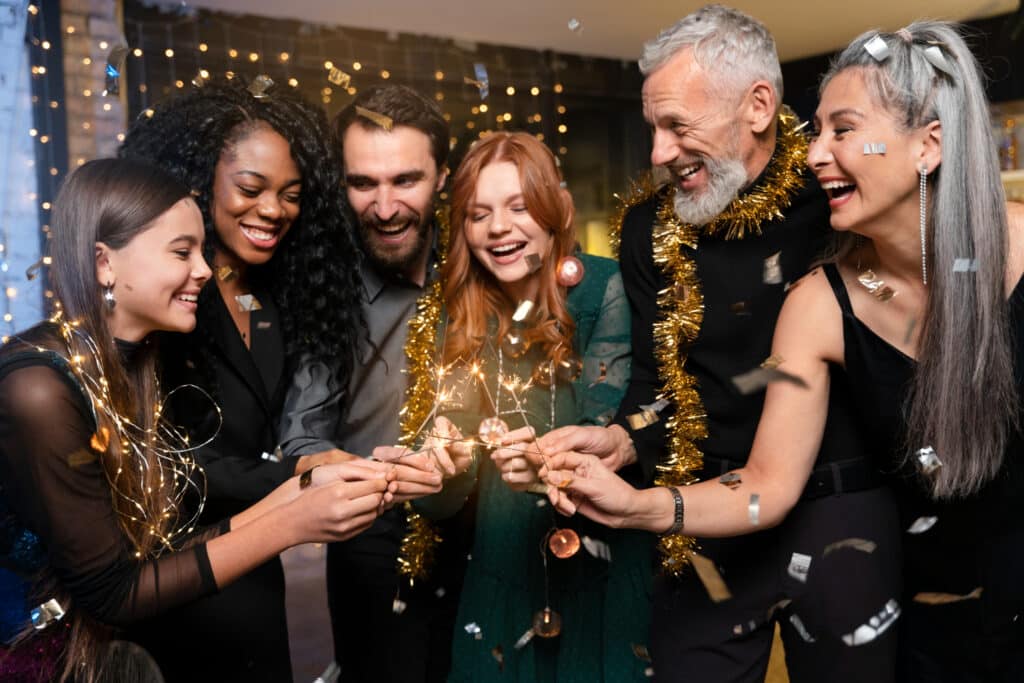 Homens e mulheres de diferentes nacionalidades segurando velas faísca enquanto sorriem.