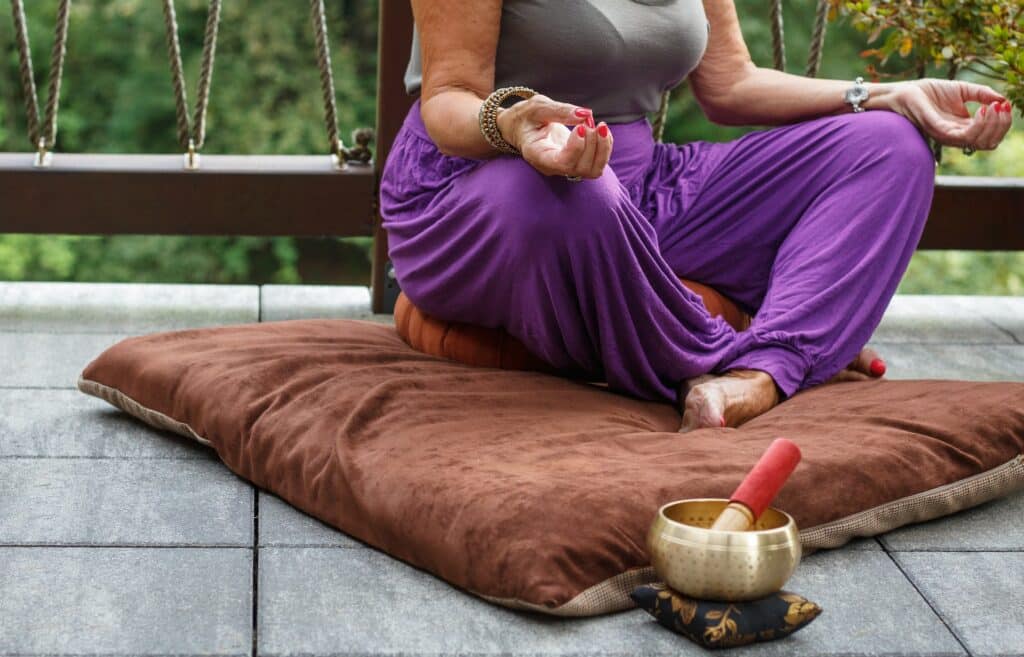 Senhora sentada sobre almofadas sobrepostas no chão. Ela une as pontas dos dedos sobre os joelhos em sinal de meditação.