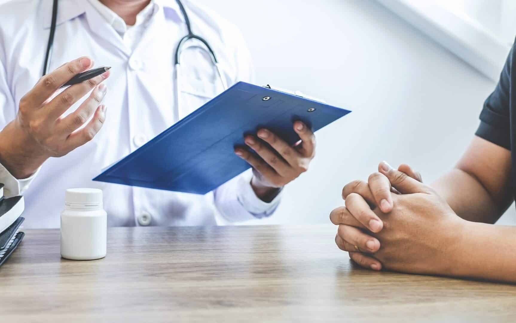 Um médico e um paciente à beira de uma mesa de um consultório.