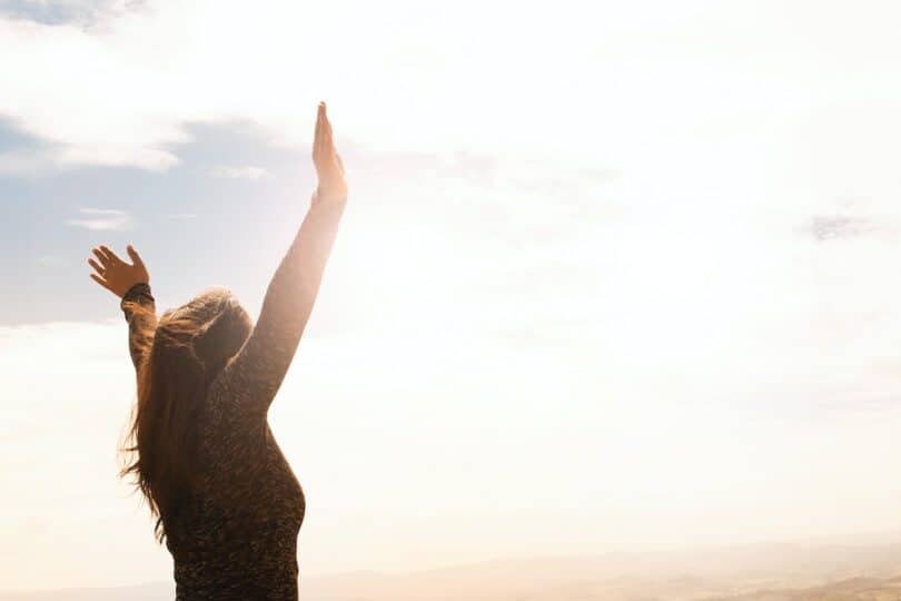 Imagem de uma mulher com os braços erguidos para o céu ensolarado.