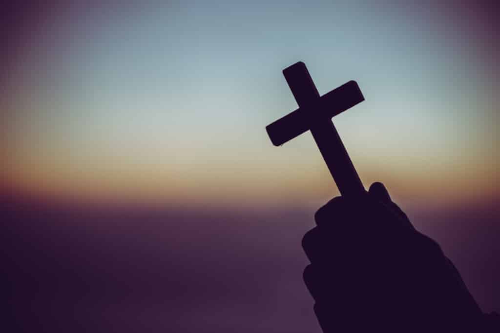 Silhueta de uma mão segurando uma cruz