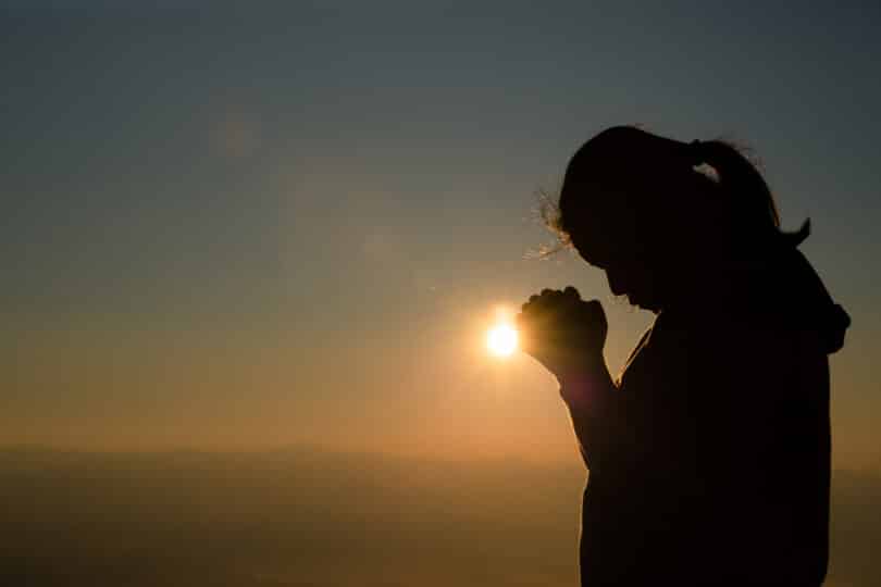 Silhueta de uma mulher orando em meio a natureza