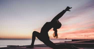 silhueta de mulher praticando yoga na praia, ao pôr do Sol.