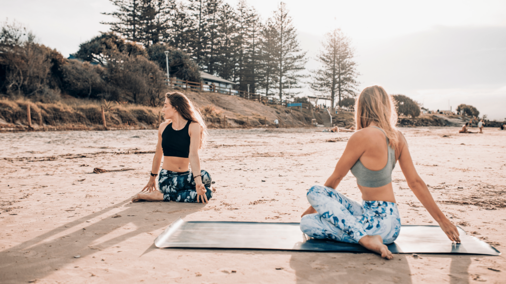 Duas mulheres praticando yoga, fazendo a pose torção.
