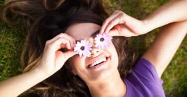 Imagem de uma mulher deitada no gramado, segurando duas flores na frente dos olhos