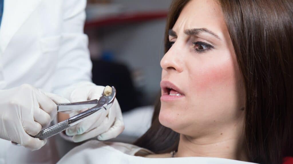 Imagem de um dentista arrancando o dente de uma pessoa que está com feição de susto