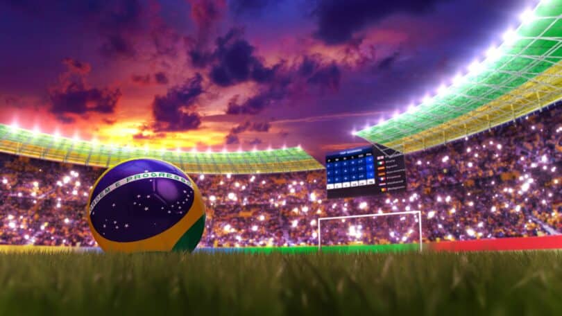 Imagem de um estádio de futebol, cheio e iluminado, e uma bola do Brasil no gramado.