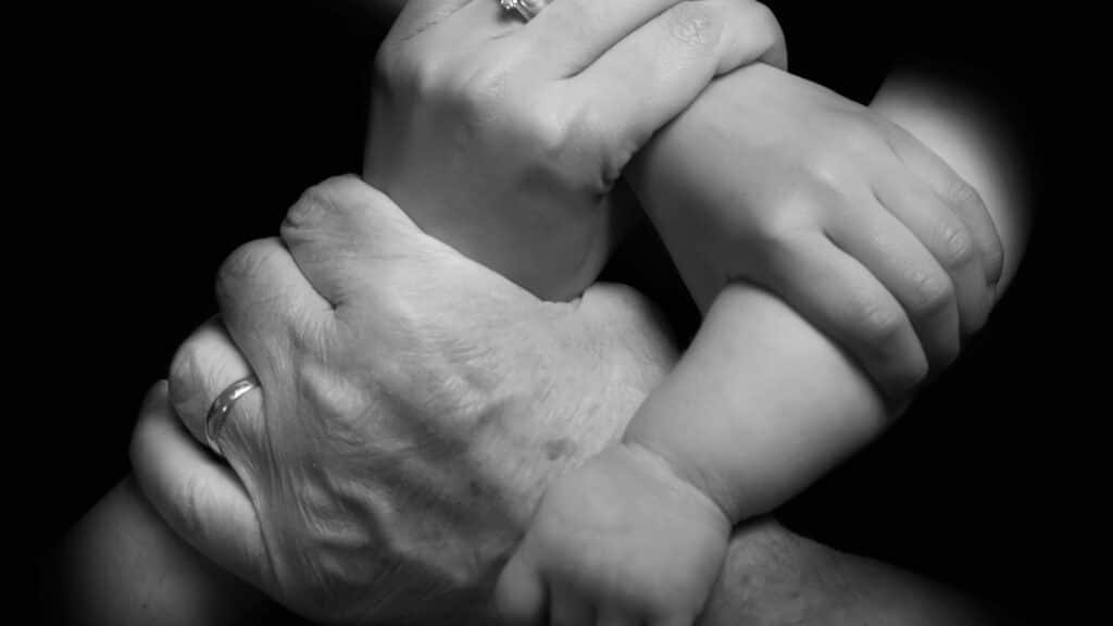 Imagem das mãos de uma família (dois adultos e duas crianças) entrelaçadas