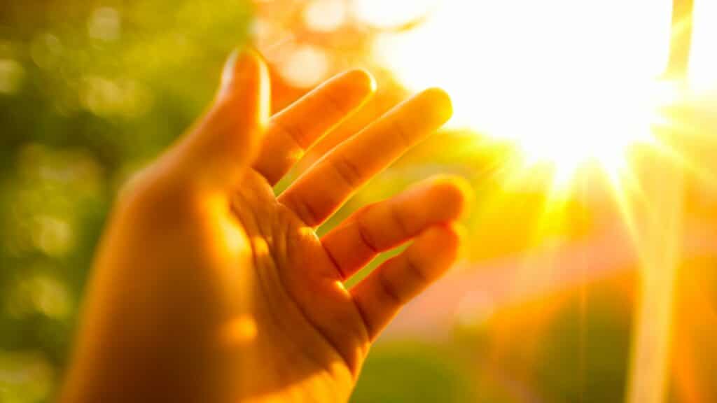 Imagem de uma mão erguida e a luz do sol refletindo sobre ela