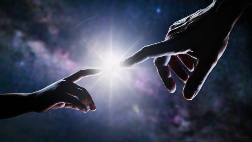 Imagem de duas mãos se encontrando, quase tocando os dedos e uma luz entre eles.