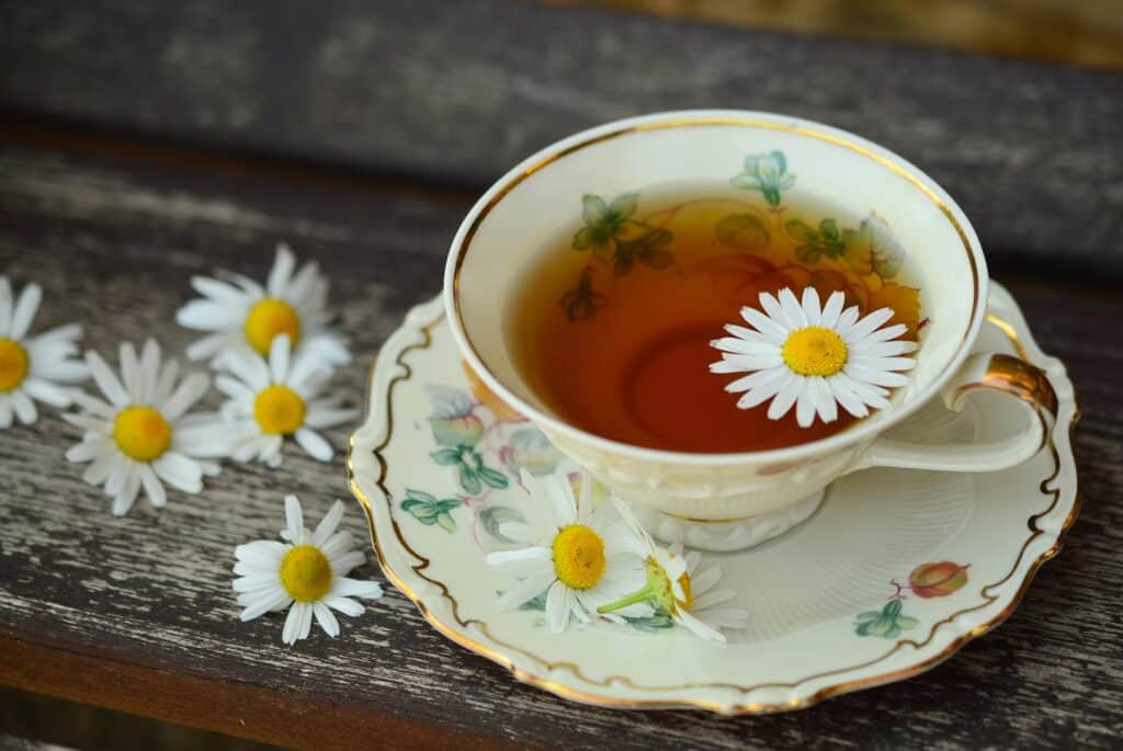 Xícara florida com chá de camomila e flores de camomila em volta.